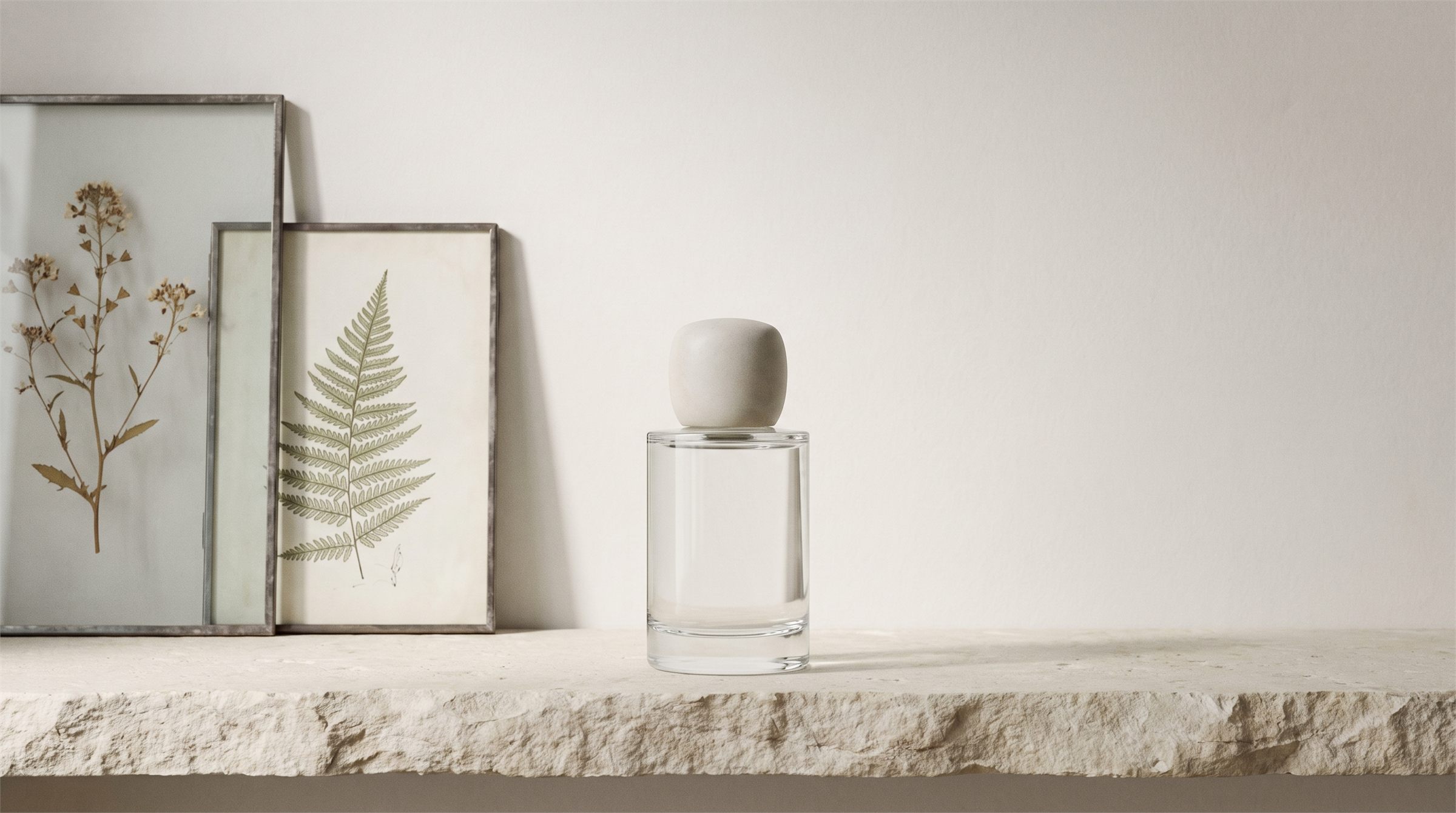 Blank glass fragrance flacon on a limestone ledge beside framed botanical prints